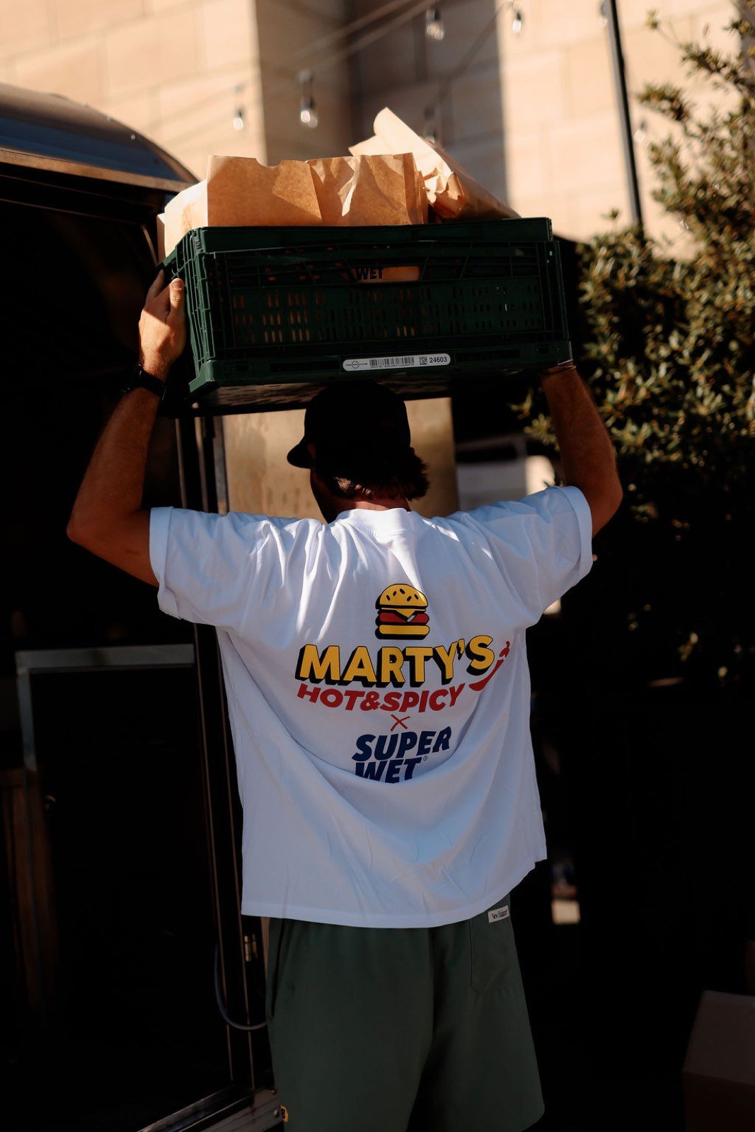 Membre de l'équipe Marty's en t-shirt Marty's Hot & Spicy x Super Wet portant une caisse de commandes lors de l'événement